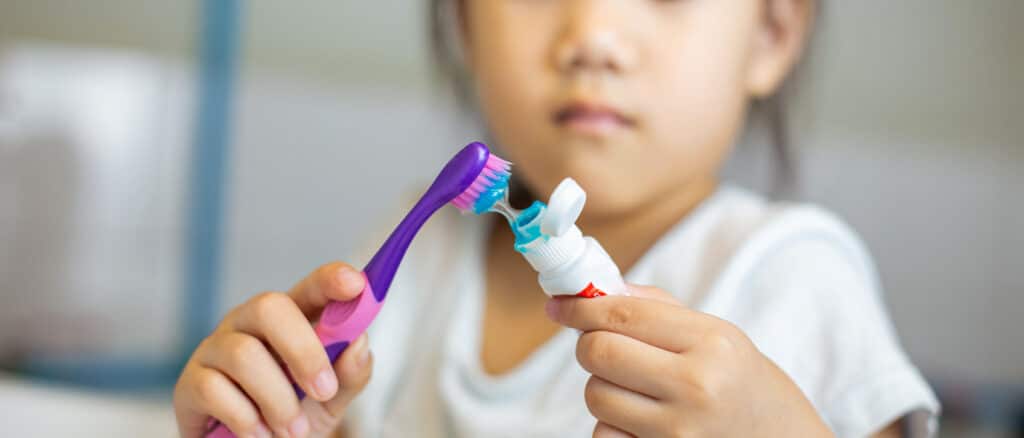 Child Putting Toothpaste on Toothbrush
