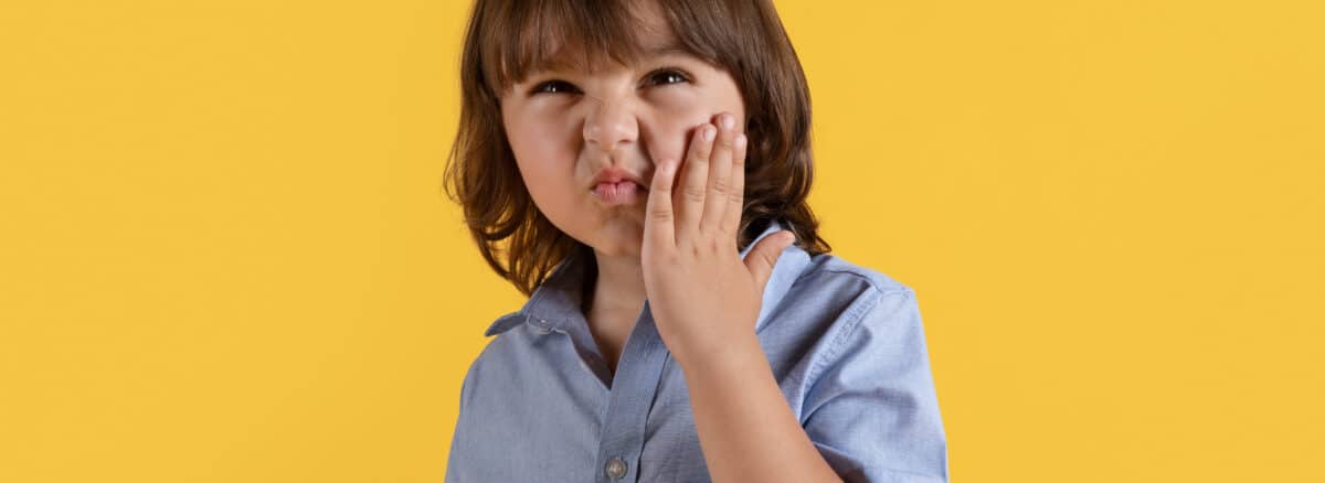 A little boy suffering from acute toothache, touching his painful cheek and frowning face