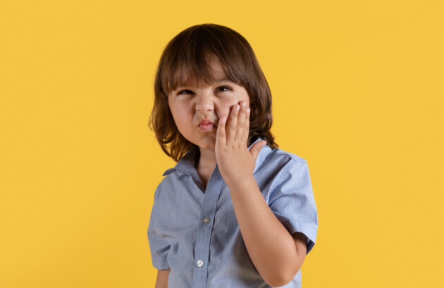 A little boy suffering from acute toothache, touching his painful cheek and frowning face