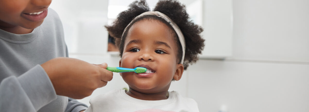 Image of a mother brushing her little daughters teeth in the bathroom at home.