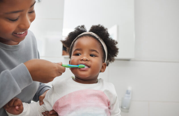 Image of a mother brushing her little daughters teeth in the bathroom at home.