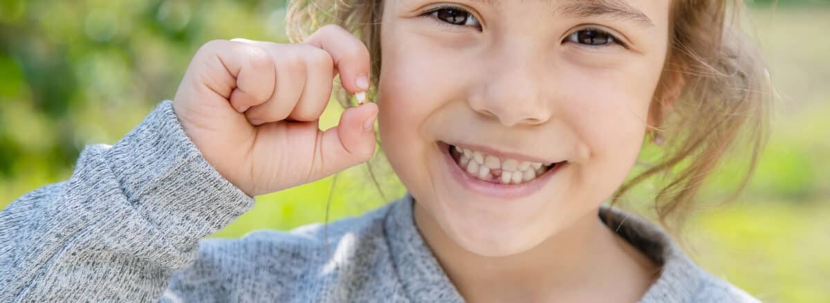 A young girl smiling and holding onto a tooth that she just lost