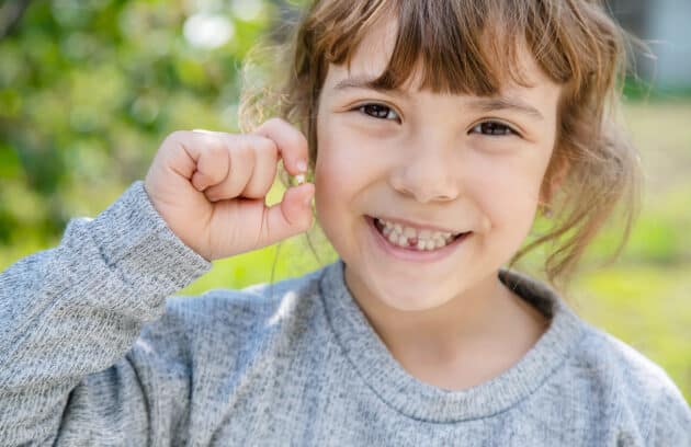 A young girl smiling and holding onto a tooth that she just lost